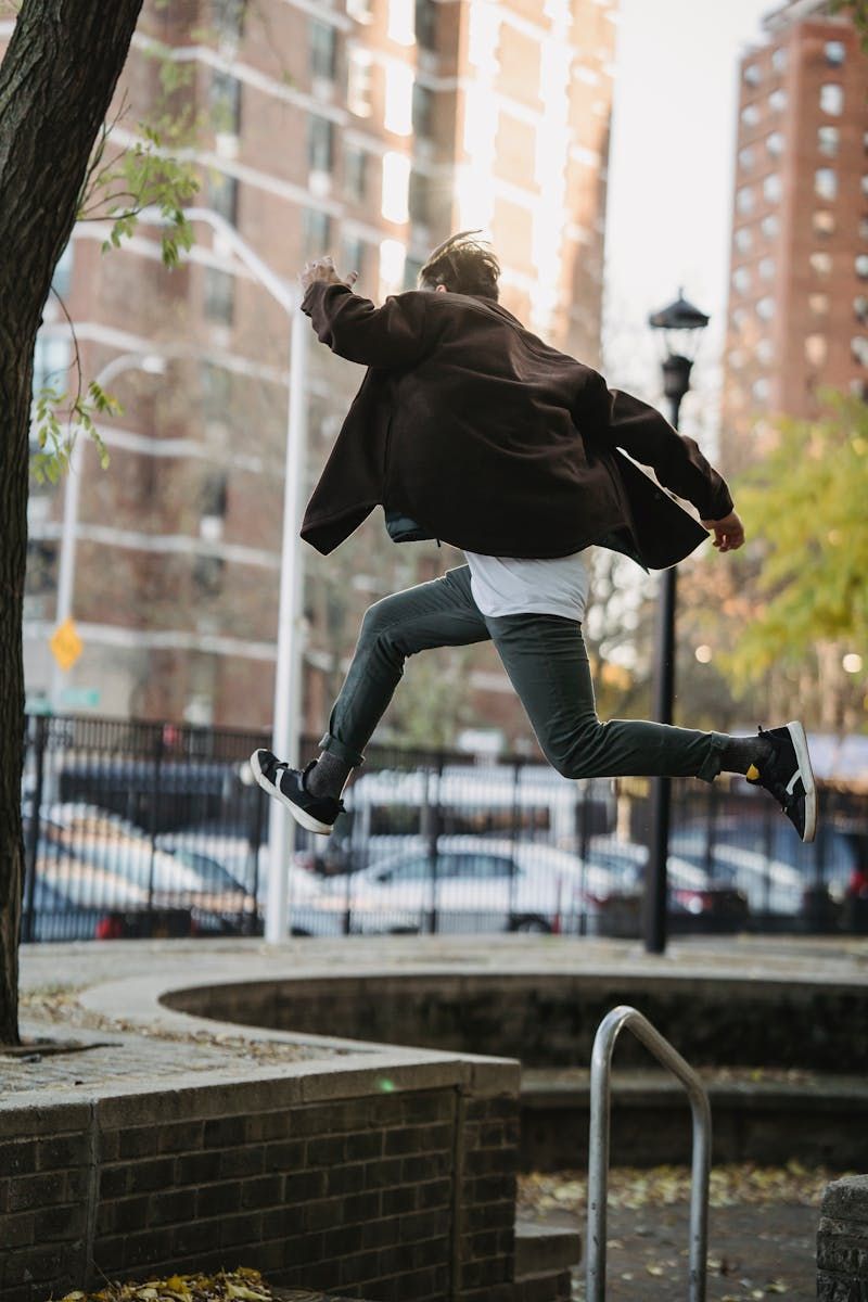 Full body back view of sportive male jumping above ground in street during parkour exercise against blurred buildings in city