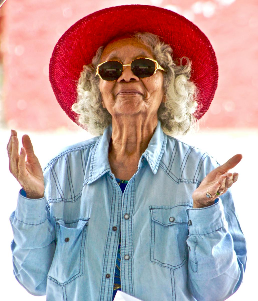 Joyful senior woman wearing a vibrant red hat and sunglasses, expressing happiness outdoors.